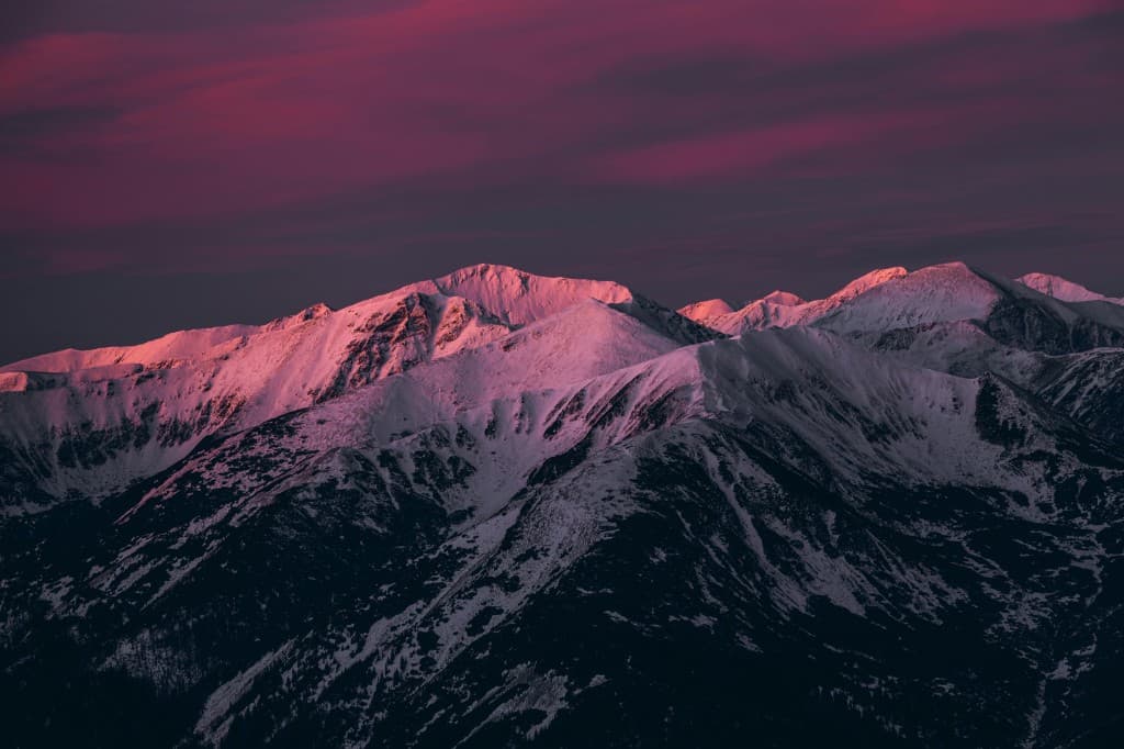 Snow-capped mountains lit by sunset against a purple sky.
