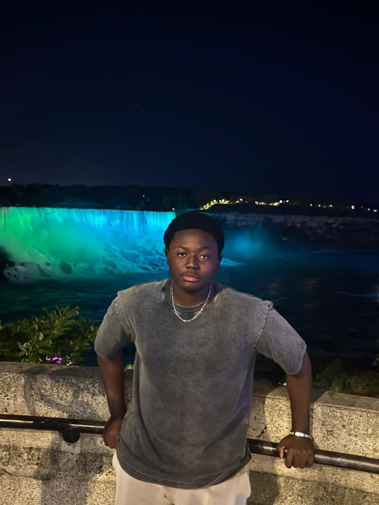 Rayann at Niagara Falls at night with the falls lit in green and blue.